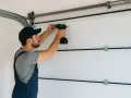Un technicien effectue la fixation moteur porte de garage avec une perceuse.