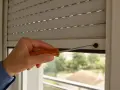 Main tenant, une personne utilise un tournevis pour réparer un volet roulant qui ne s'ouvre pas complètement.