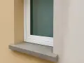Une pose fenêtre sur appui de fenêtre en pierre grise, avec un mur extérieur texturé beige et un mur blanc cassé.