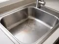 Évier en inox taché par acide, montrant des marques de corrosion sur le fond.