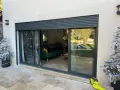 Volet battant alu RAl 7016, moderne, protégeant une baie vitrée donnant sur un salon et une piscine.