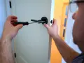 Un homme utilise un tournevis pour changer une poignée de porte ancienne pour un modèle moderne.
