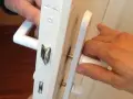 Deux mains actionnent une poignée de porte qui grince, révélant le mécanisme de serrure blanc.