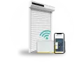 Installation domotique volet roulant : un volet blanc, une box Somfy et un smartphone affichant l'application de contrôle.