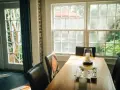 Le **couleur encadrement fenêtre intérieur** blanc met en valeur la lumière naturelle baignant la salle à manger. Des chaises en cuir marron entourent une table en bois.
