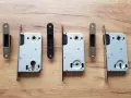 Ensemble de serrures pour porte intérieure, avec leurs gâches argentées et noires, sur fond de bois.