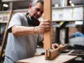 Artisan assemble des pièces de bois pour fabriquer une fenêtre. Il tient une pièce verticale et la joint à une autre pièce.