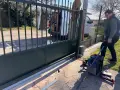 Un homme installe le moteur d'un portail coulissant. Des outils sont posés au sol près de la cellule.