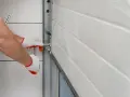 Main tenant avec des gants blancs et rouges, manipule un mécanisme pour comment ouvrir un portail électrique manuellement.