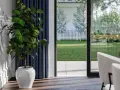 Vue sur jardin verdoyant depuis une pièce, avec un ficus en pot près du détail seuil porte fenêtre.