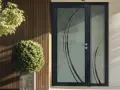 Porte d'entrée moderne avec un type de vitrage décoratif aux motifs courbes. Un arbuste et un arbre apportent une touche de verdure.