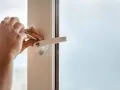 Main tenant utilise un tournevis pour changer la poignée d'une fenêtre en aluminium.