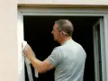 Pose d'une fenêtre en rénovation sur ancien dormant. L'ouvrier nettoie le cadre avec un chiffon.