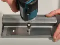 Utilisation d'une visseuse pour fixer une plaque métallique, étape clé pour ouvrir une porte aimantée.