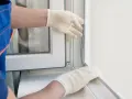 Mains gantées ajustant un joint lors du remplacement d'une fenêtre.