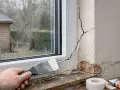 Application d'enduit sur une fissure près d'une fenêtre. Un outil de maçonnerie est utilisé pour réparer le mur extérieur.