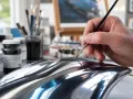 Main d'artiste peignant un objet à la finition chrome, ajoutant des détails subtils pour un réalisme saisissant.