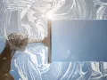 Nettoyage d'une vitre avec une raclette et de la mousse. Le soleil brille à travers la surface savonneuse, créant des reflets. Idéal pour enlever la colle sur vitre.