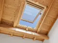 Un *uw velux* ouvert sur un ciel bleu éclatant, encadré par des poutres et un plafond en bois chaleureux.