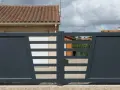 Portail solaire ne fonctionne plus. La grille grise moderne, avec ses lames horizontales et son design asymétrique, est fermée devant une maison.