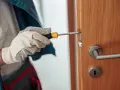 Main tenant utilise un tournevis pour réparer une serrure qui coince sur une porte en bois.