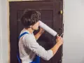 Un homme utilise une mousse expansive pour isoler une porte en bois.
