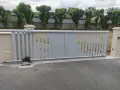 Portail électrique gris coulissant, avec son moteur discret, assure la protection du domicile. Des arbres taillés bordent la propriété.