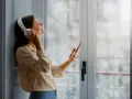 Une femme écoute de la musique avec des écouteurs, profitant du calme malgré la pluie. Un film isolant phonique pour fenêtre pourrait améliorer cette quiétude.