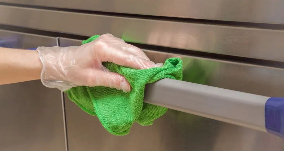 Main tenant nettoie avec un chiffon vert un acier inoxydable doré, gardant une hygiène impeccable.