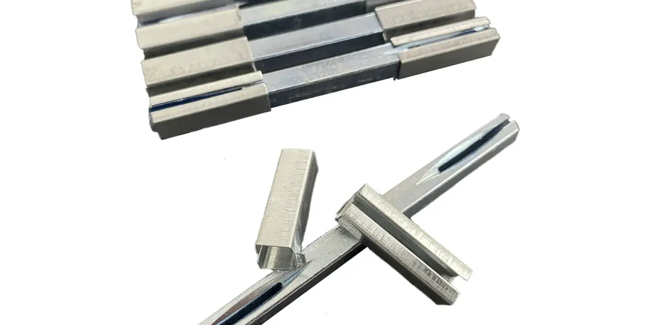 Ensemble de pièces métalliques, dont un carré de serrure, disposées sur fond blanc.
