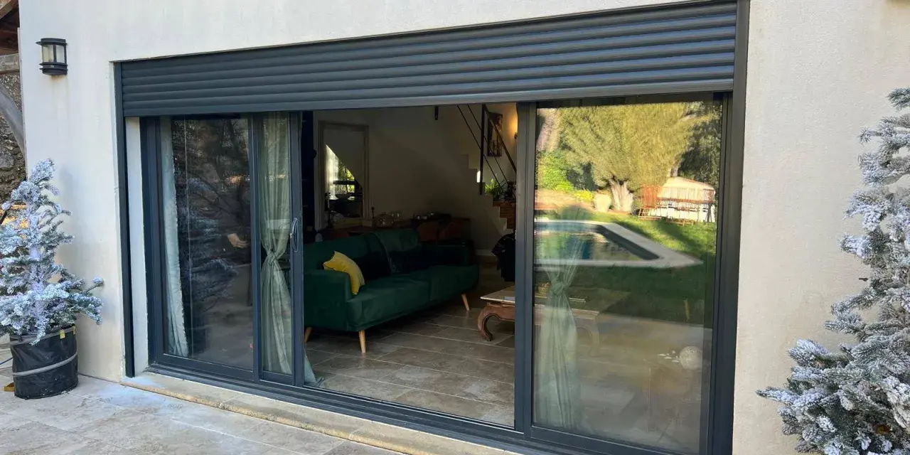 Volet battant alu RAl 7016, moderne, protégeant une baie vitrée donnant sur un salon et une piscine.