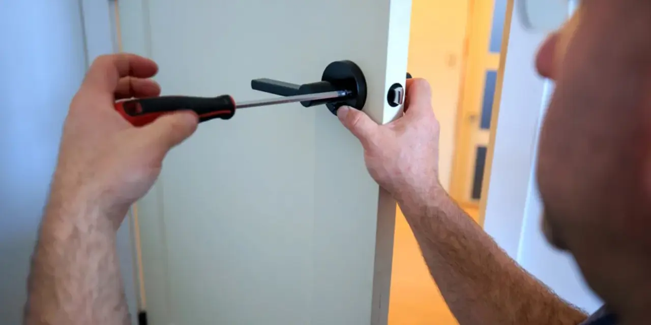 Un homme utilise un tournevis pour changer une poignée de porte ancienne pour un modèle moderne.