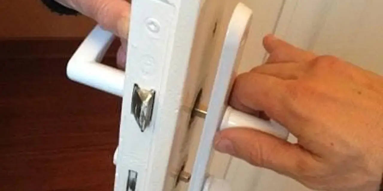Deux mains actionnent une poignée de porte qui grince, révélant le mécanisme de serrure blanc.