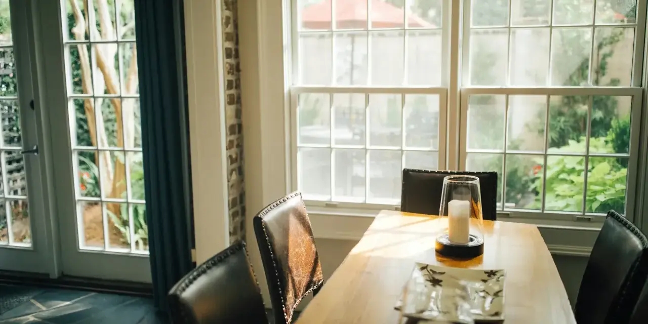 Le **couleur encadrement fenêtre intérieur** blanc met en valeur la lumière naturelle baignant la salle à manger. Des chaises en cuir marron entourent une table en bois.