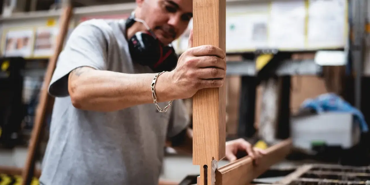 Artisan assemble des pièces de bois pour fabriquer une fenêtre. Il tient une pièce verticale et la joint à une autre pièce.