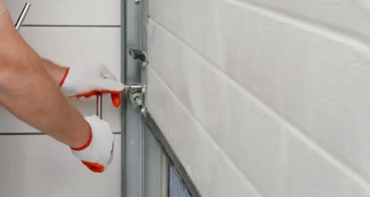 Main tenant avec des gants blancs et rouges, manipule un mécanisme pour comment ouvrir un portail électrique manuellement.