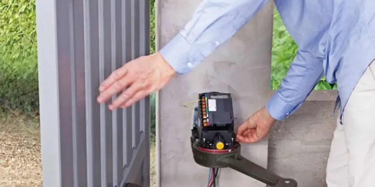 Un homme ajuste le moteur d'un portail électrique bloqué ouvert.