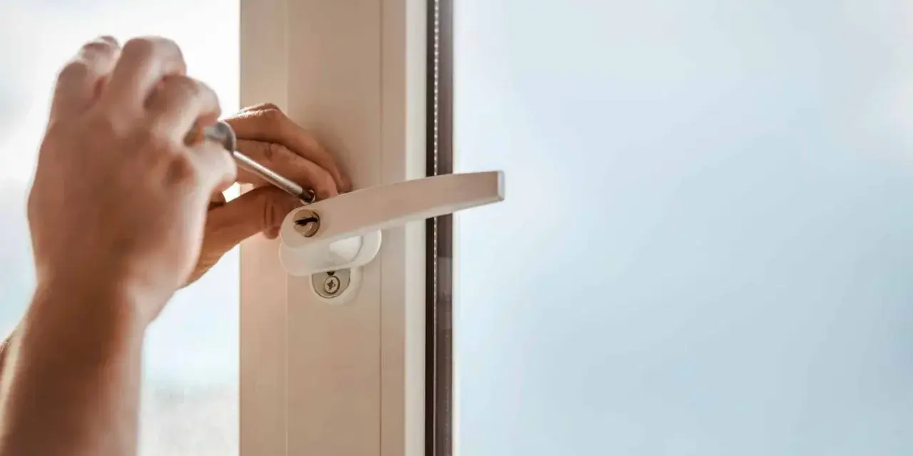 Main tenant utilise un tournevis pour changer la poignée d'une fenêtre en aluminium.