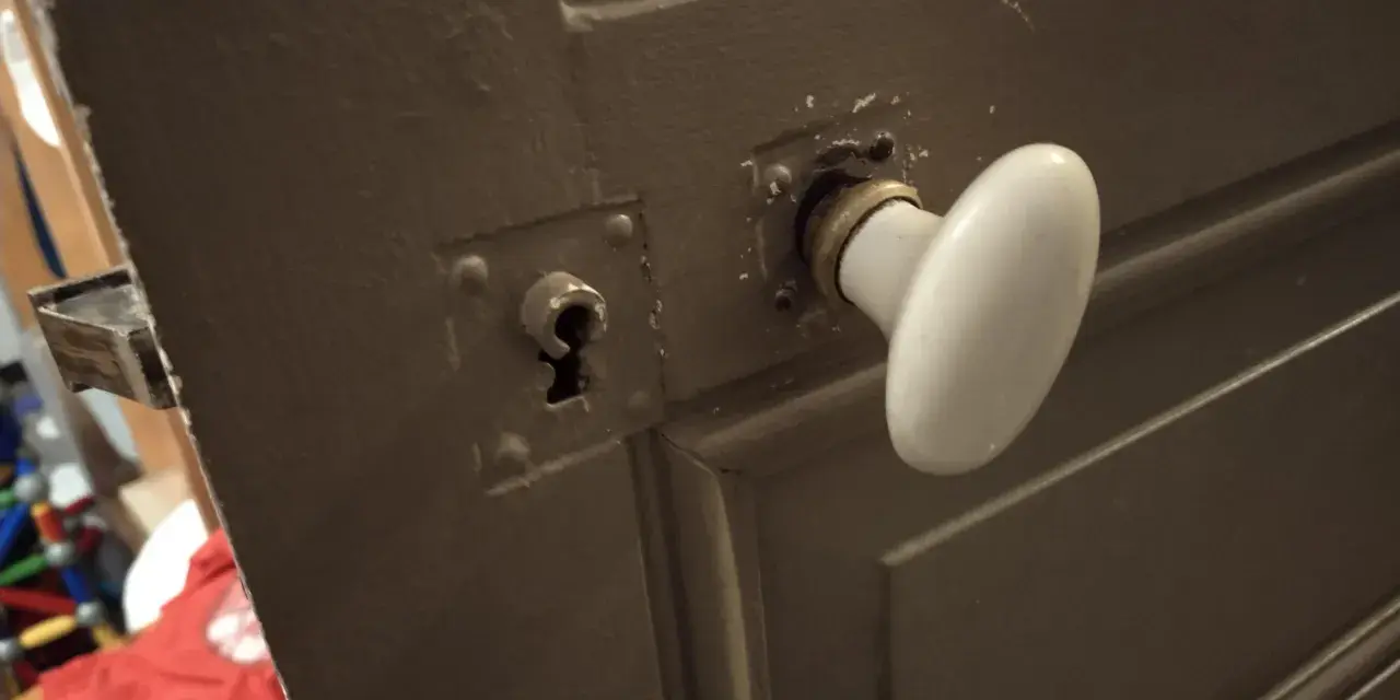 Détail du mécanisme poignée porte ancienne avec une rosace et une serrure visible.