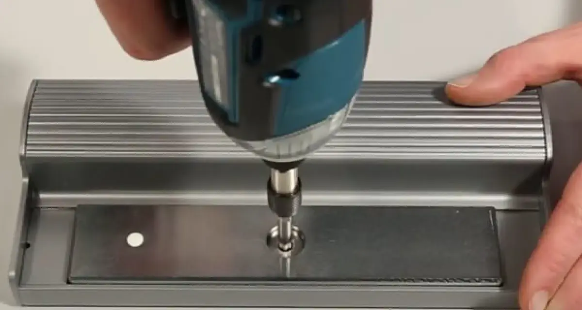 Utilisation d'une visseuse pour fixer une plaque métallique, étape clé pour ouvrir une porte aimantée.