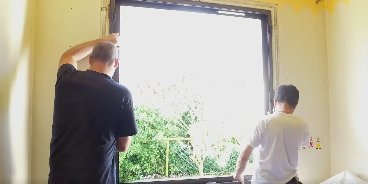 Deux hommes installent une nouvelle fenêtre, une étape clé dans la rénovation de cette pièce.