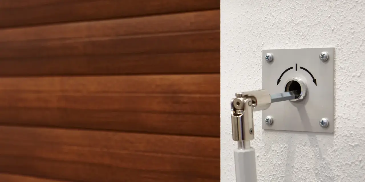Mécanisme pour comment ouvrir une porte de garage électrique de l'extérieur. Un levier est inséré dans une serrure sur un mur blanc, à côté d'une porte en bois.