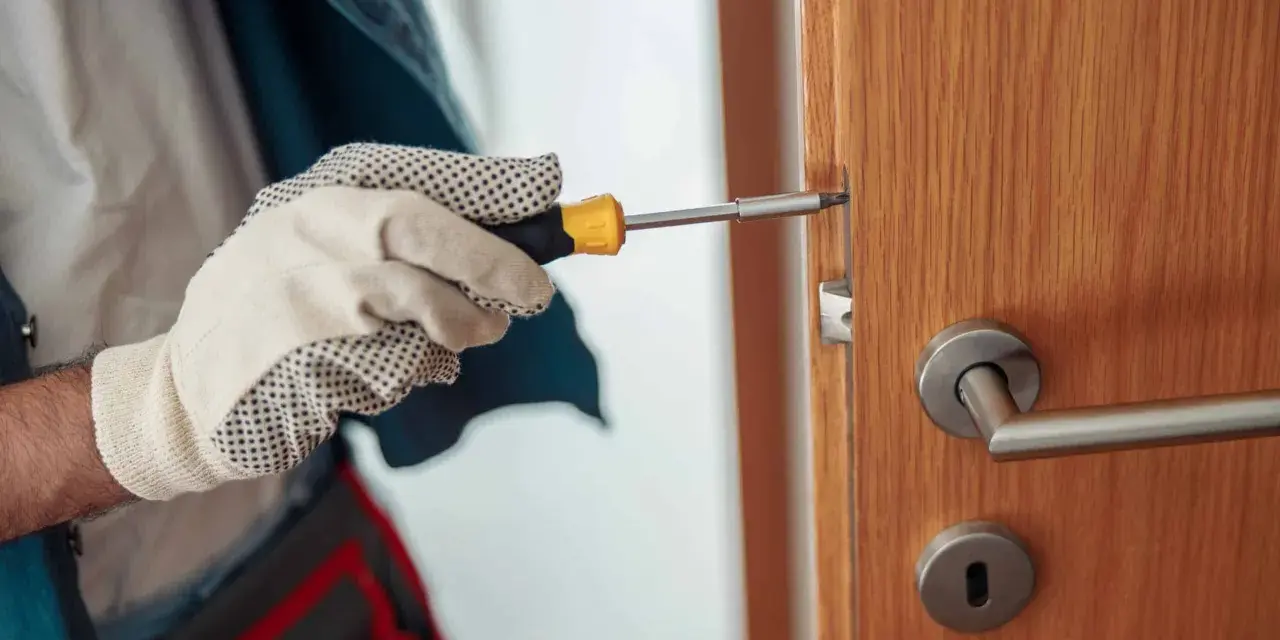 Main tenant utilise un tournevis pour réparer une serrure qui coince sur une porte en bois.