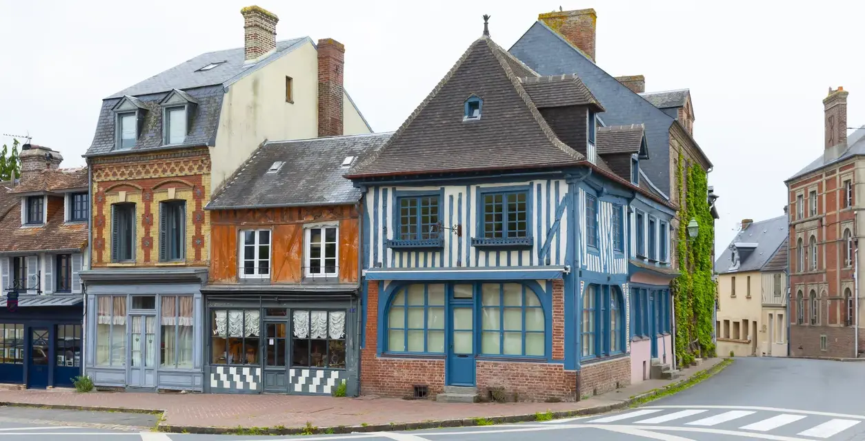 Façades colorées de maisons anciennes, dont une à colombages bleus et blancs. Une description d'une fenêtre ancienne orne la façade orange.