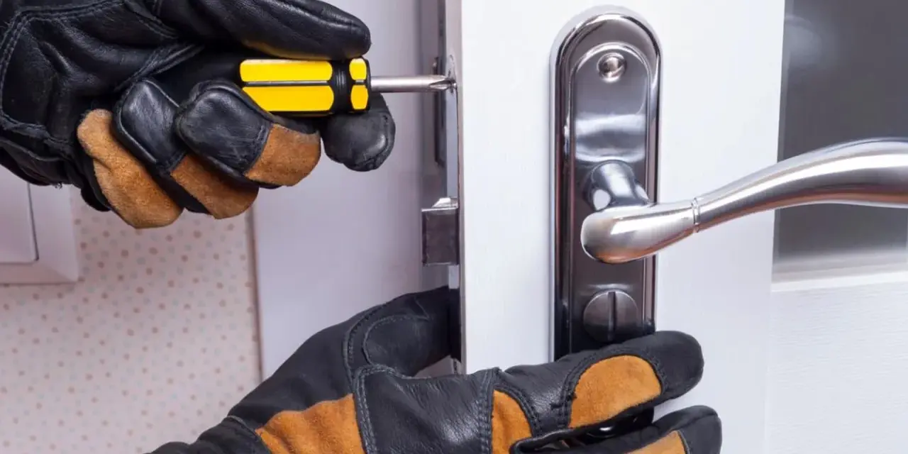 Mains gantées ajustent un loquet serrure bloqué sur une porte blanche avec un tournevis.