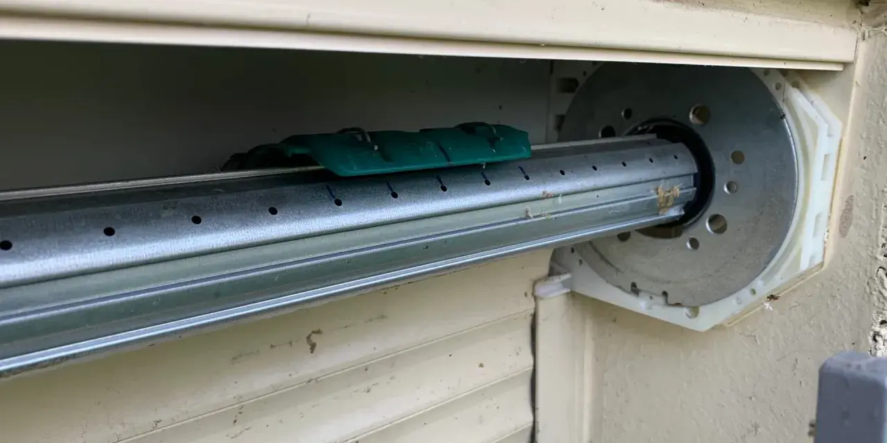 Détail du mécanisme d'un volet roulant, prêt pour comment démonter un moteur de volet roulant. Le tube métallique est visible, avec un support vert.