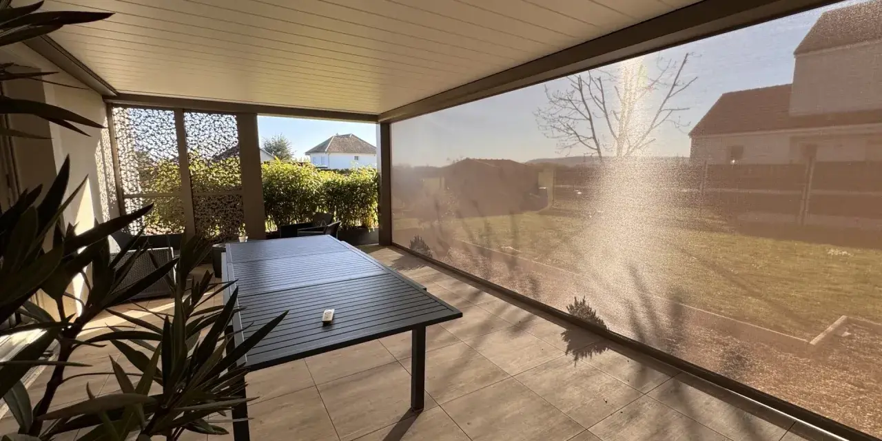 Terrasse avec table et chaises, sous un abri moderne. La menuiserie RAL 7006 s'intègre parfaitement au paysage.