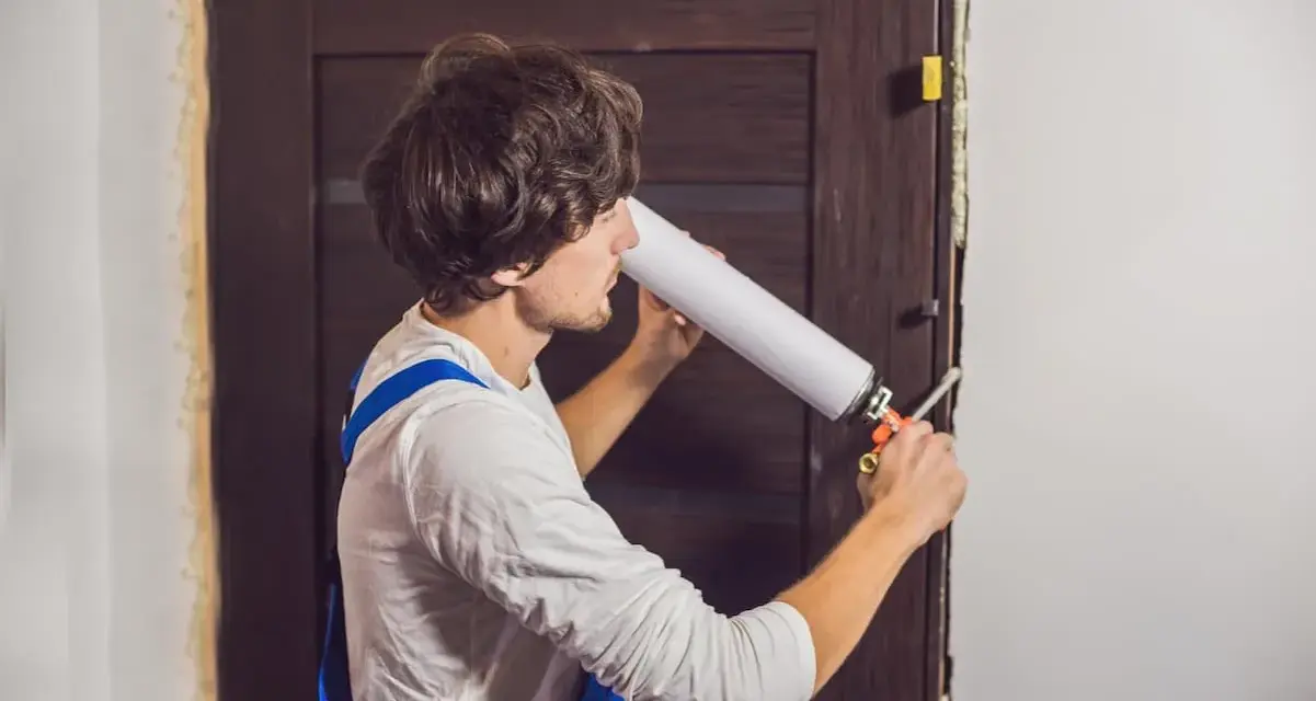 Un homme utilise une mousse expansive pour isoler une porte en bois.