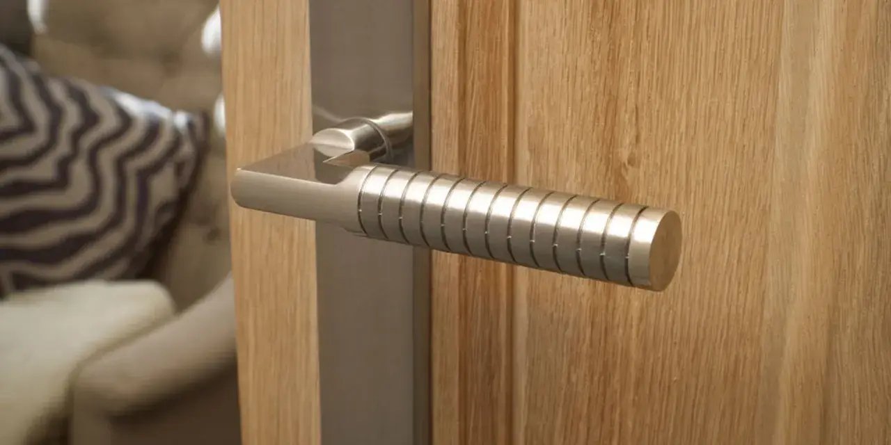 Poignée de porte d'entrée en métal brossé, au design moderne avec un manche texturé, fixée sur une porte en bois clair.