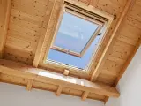 Un *uw velux* ouvert sur un ciel bleu éclatant, encadré par des poutres et un plafond en bois chaleureux.